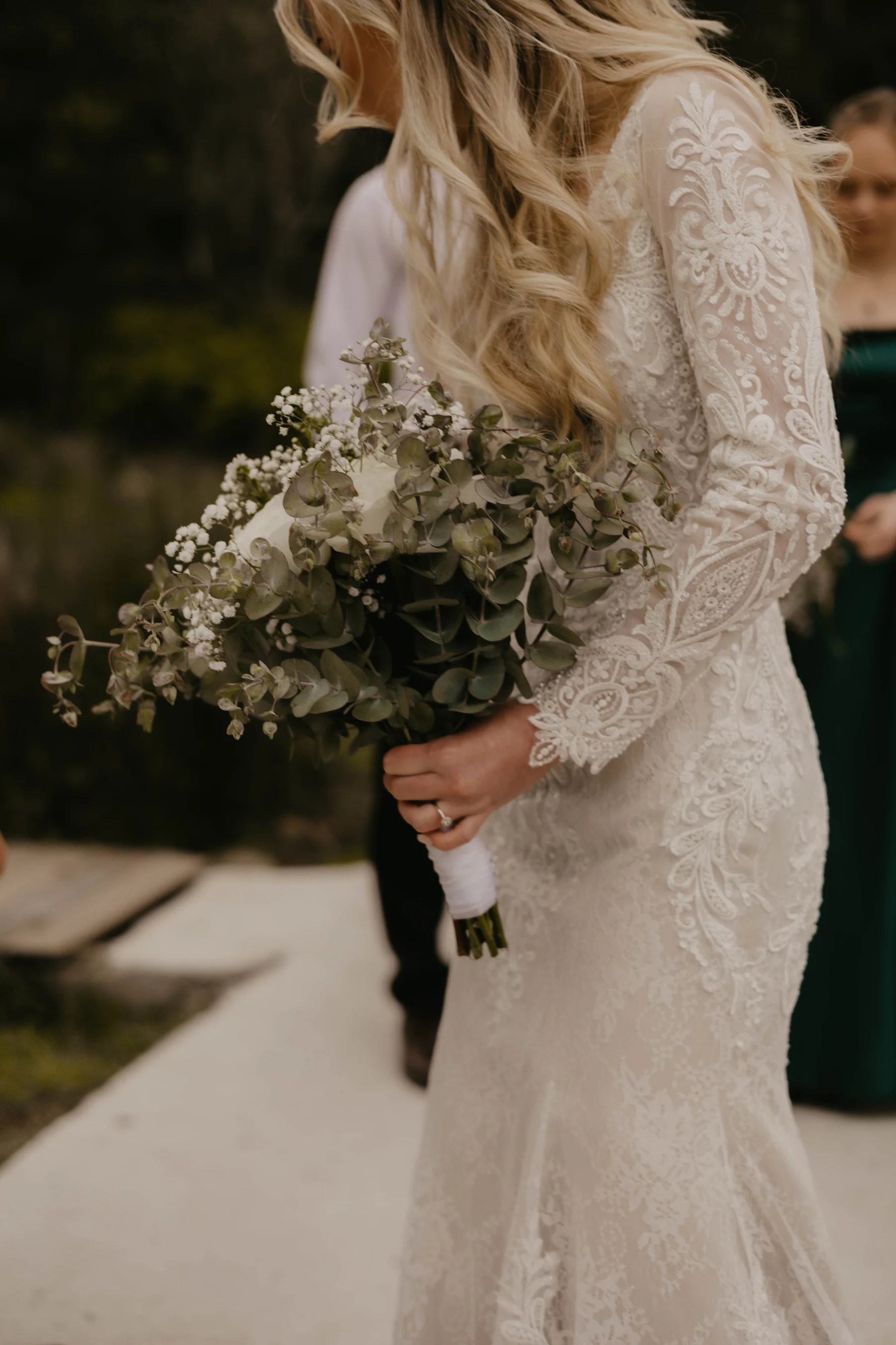 Bride in a lace wedding dress holding a eucalyptus and white flower bouquet